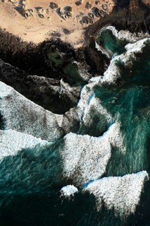 Aerial view of frothy ocean waves meeting the distinct rocky shores of Popcorn Beach in