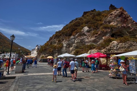 A lively square with tourists and colorful umbrellas against a rocky backdrop, Vulcano Lipari