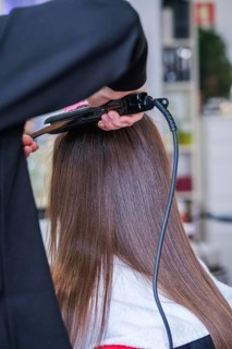 A hair stylist uses a flat iron to perform keratin hair straightening in a beauty salon. The