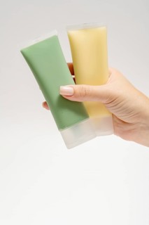 Cropped unrecognizable person showcasing two skincare tubes, a green mask with spirulina, kaolin,