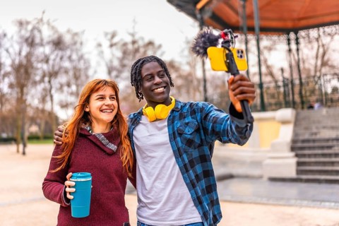 Two young content creators are recording a video blog using a smartphone with a microphone in a