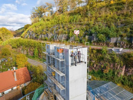 Workers on a towering building next to a hill, in the midst of autumnal nature, extension of the