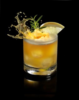 An ice cube cube falls into a tumbler and allows the liquid to splash on, studio shot against a