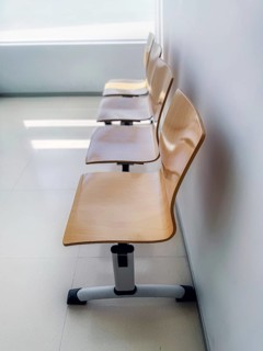A row of minimalist, light wood chairs lines a clean, bright waiting area. The simple design