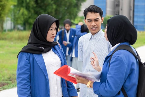A group of Asian Muslim students in blue uniforms engaging in a conversation outdoors. They stand