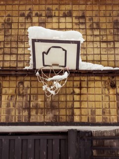 A basketball hoop laden with snow, backed by a grid of brown tiles, evoking urban wintertime