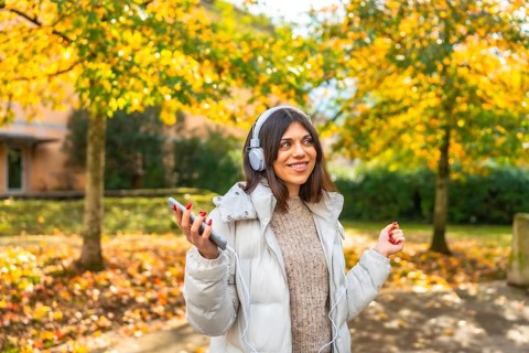 Caucasian beauty woman listening to music and dancing in the city park during a sunny day of autumn