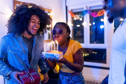 African young cool woman blowing candles of birthday cake with multi-ethnic friends at home