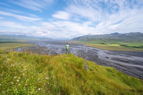 Hiker, young man on a hill, view over alluvial land, meandering river, Dímonarhellir, Suðurland,