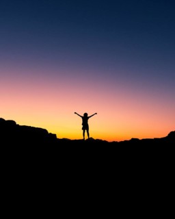Happy celebrating winning success woman at sunset or sunrise standing elated with arms raised up in