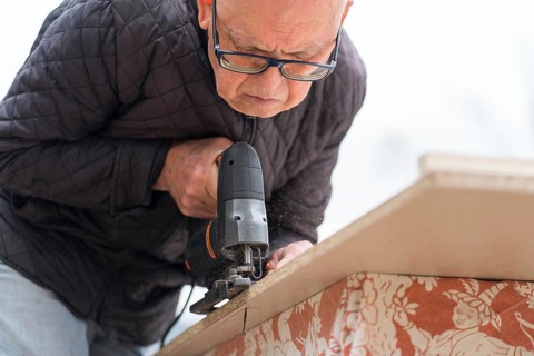 From below senior man focused on using a jigsaw for carpentry projects, showcasing meticulous work