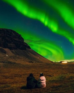 Two people romantic couple sitting under vivid aurora borealis with northern landscape, magical