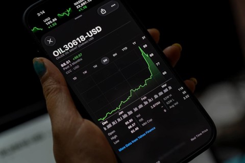In this photo illustration, a person looks at a smartphone displaying Brent crude oil prices in