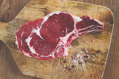 Raw rib eye steak, cowboy steak, on a wooden chopping board, top view, no people