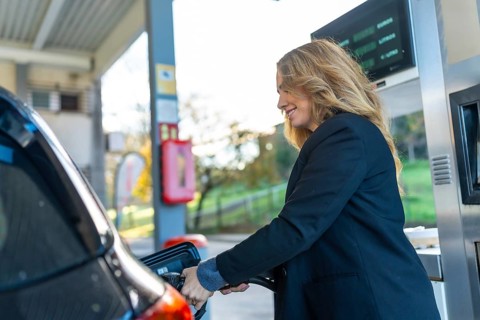 Woman refueling her car at a gas station, smiling while holding the pump nozzle everyday routine of