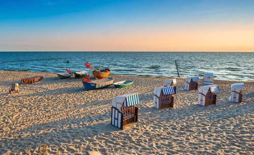 Beach chairs and fishing boats with red flags on fine sandy beach at sunrise, Baltic resort