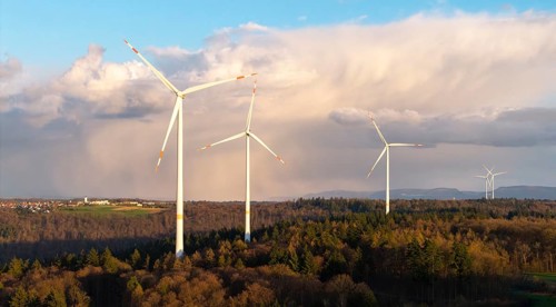 Wind turbines stand in a wooded landscape with dramatic clouds in the background, wind turbine,