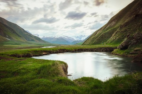 Scenic Truso Valley in Georgia with winding river, green meadows, and Caucasus mountains in