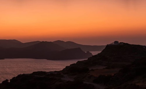 A captivating sunset over Milos Island, Greece, with the silhouette of hills and the vibrant orange