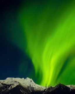 Brilliant green aurora borealis glowing above snowy mountain peaks under starry night sky, symbol