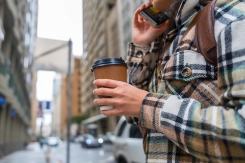 Woman standing on an urban street, holding a disposable coffee cup and making a call on a mobile