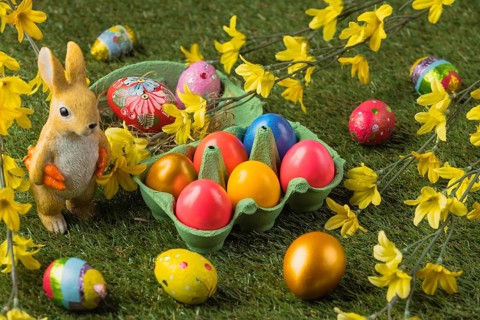 An Easter bunny figure next to colorful Easter eggs and bright blossoms on a green background
