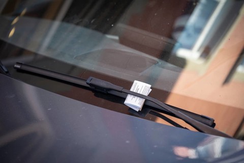 A speeding ticket, also known as a parking ticket, stuck to a car windshield wiper due to incorrect