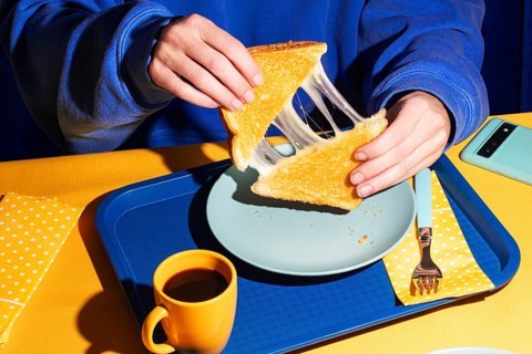 Overhead view of a person in a blue sweatshirt holding a crispy grilled cheese sandwich. Harsh