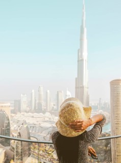 Back view of female traveler in a sunhat on a high-rise balcony looking toward Burj Khalifa and