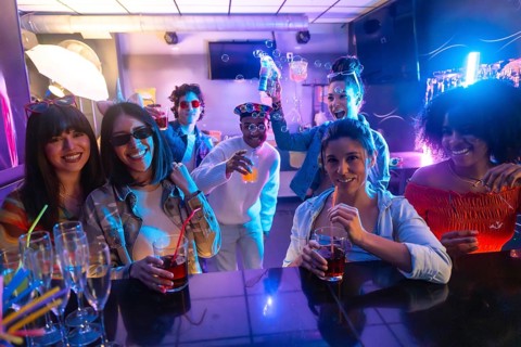Group of diverse young adults laughing, smiling, and enjoying drinks and bubbles at a vibrant