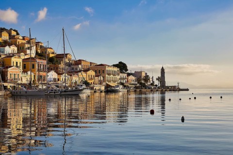 Lively harbour town with buildings reflecting in the water and a lighthouse. Tranquil Mediterranean