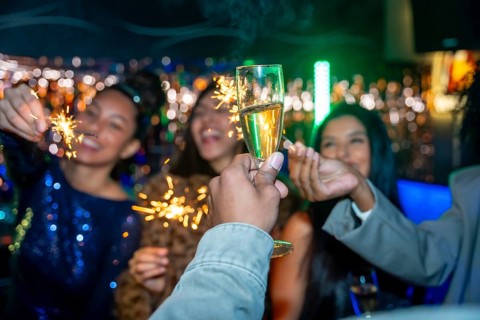 Group of diverse young adult friends toasting with champagne glasses and holding sparklers while