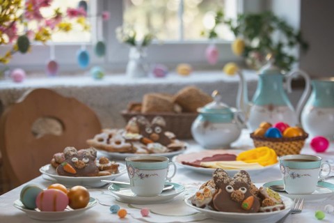 Breakfast table with Easter eggs, cookies, pastries and a cold plate in front of a decorated window