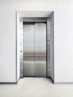 A sleek, stainless steel elevator door set in a modern hallway. The minimalist design and neutral