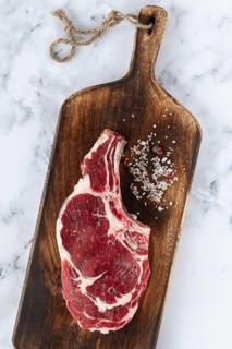 Raw rib eye steak, cowboy steak, wooden chopping board, marble table, top view, no people