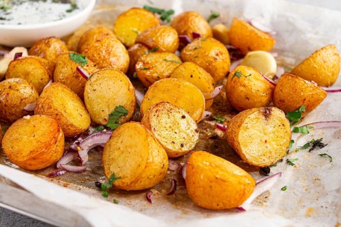 Roasted potatoes sit on a baking sheet next to chopped herbs and red onions. They are golden brown