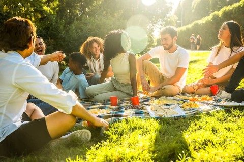 Rays of the sun illuminating multi-ethnic friends sitting on blanket enjoying a picnic in a park