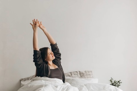 A woman stretches energetically in bed, embracing wellness. Her morning routine symbolizes health,