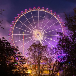 A large, brightly lit Ferris wheel with colourful lights against a night sky and surrounded by