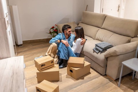 Young couple taking a break from unpacking, embracing amidst moving boxes in their new home,