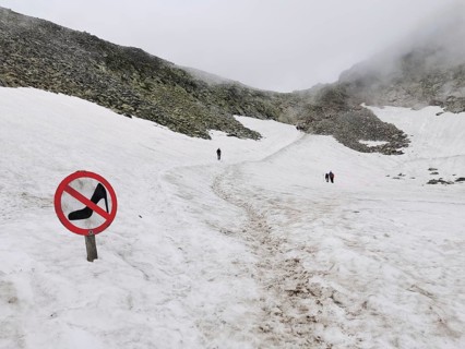 People walk across a snow-covered mountain field with warning sign, no high heels, high heels,