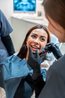 Dentist wearing black gloves using dental tools examining smiling patient's teeth in modern dental