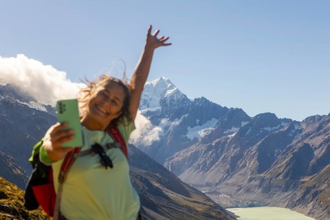 A joyful woman captures a selfie while experiencing the crisp autumn air on Mount Cook, New Zealand
