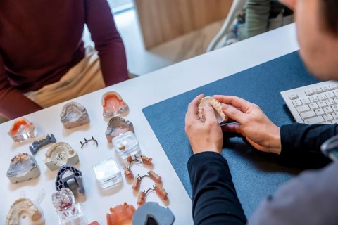 Dentist explaining to patient treatment with dental prosthesis, surrounded by various dental models