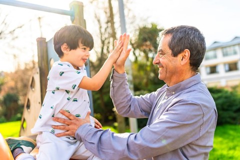 Grandfather and grandson are giving high five at the playground, enjoying a sunny day together