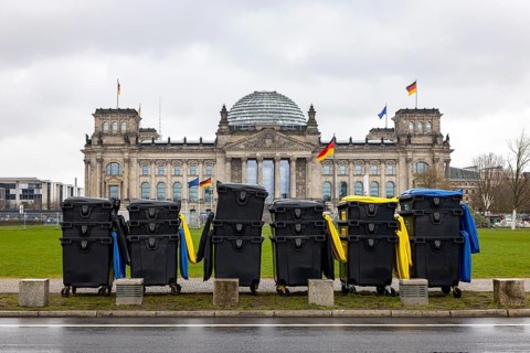 Reichstag Berlin with waving German flags. There are dumpsters from a major event in front of it.