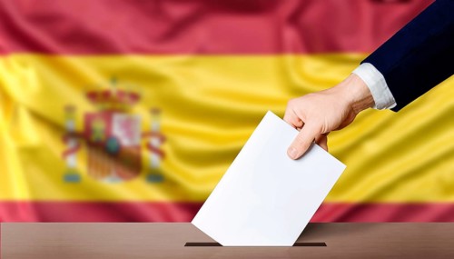 Spain general elections, voting concept. Hand holding ballot in the ballot box with the flag of