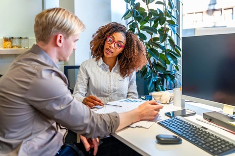 Two coworkers, a man and a woman, are discussing charts and data in a modern coworking office,