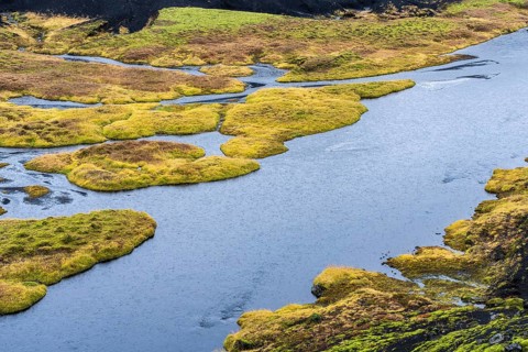 An aerial view of an Icelandic riverside captures dynamic water flow surrounded by vibrant green