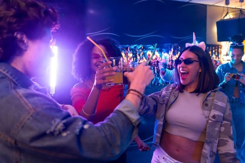 Group of young diverse friends enjoying an exciting night out, cheering with cocktails and dancing